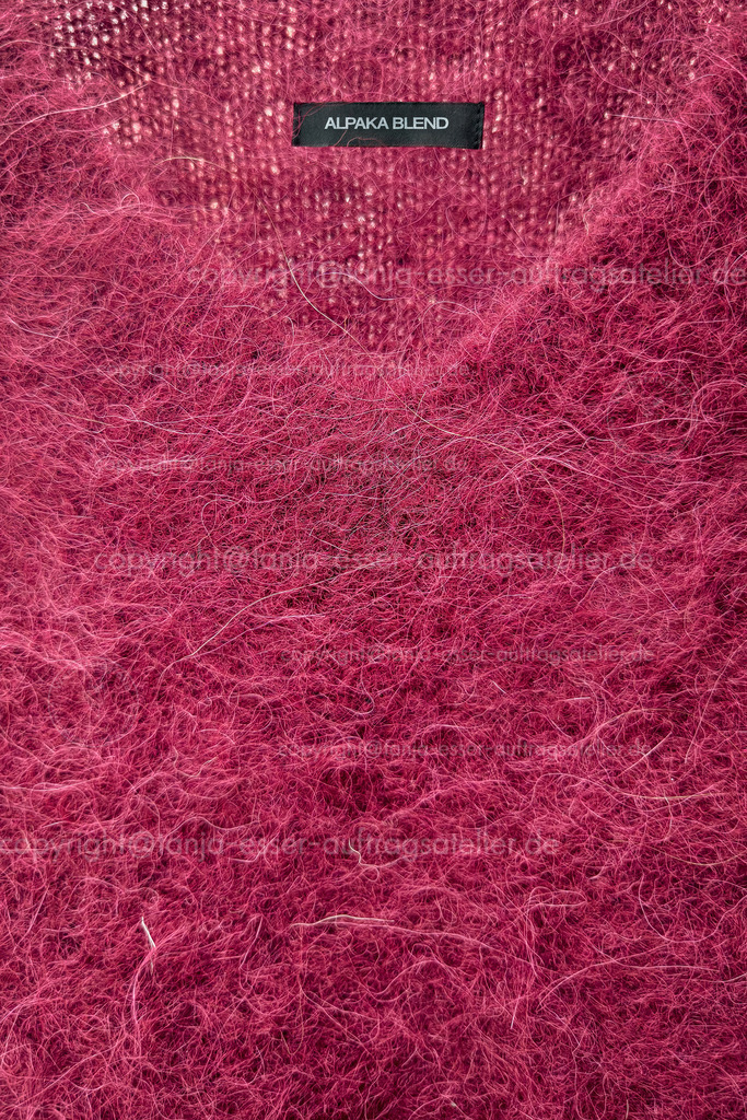 Alpaka Pullover D | Leuchtend bordeauxfarbener V Ausschnitt Pullovers mit einem Etikett, das den englischen Text Alpaka Mischung kennzeichnet. Die Oberfläche ist flauschig und mit langen Fasern, charakteristisch für Alpakamischungen. 