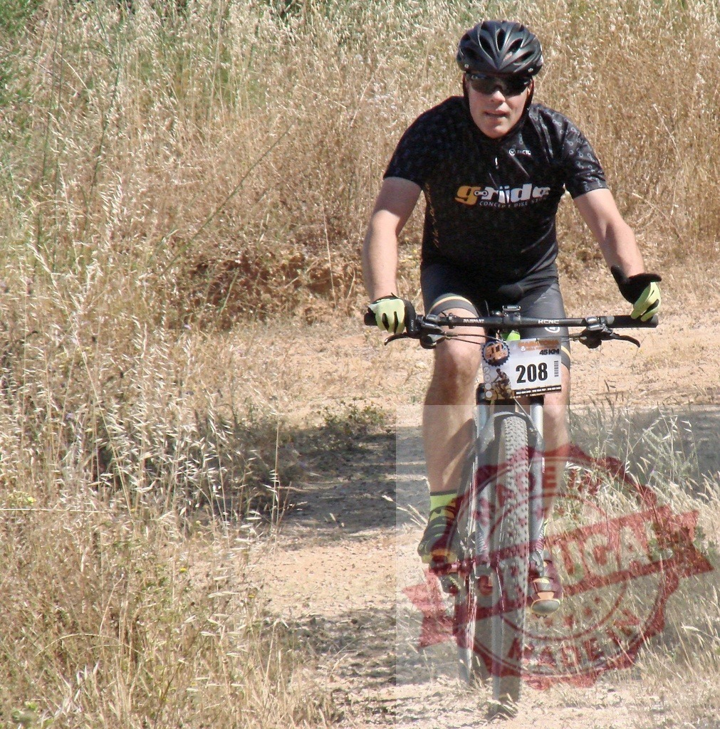 Cyclist riding mountain bike on dirt road near tall grass | Male cyclist wearing helmet and gloves riding mountain bike on dirt road near tall grass - Realized with Pictrs.com