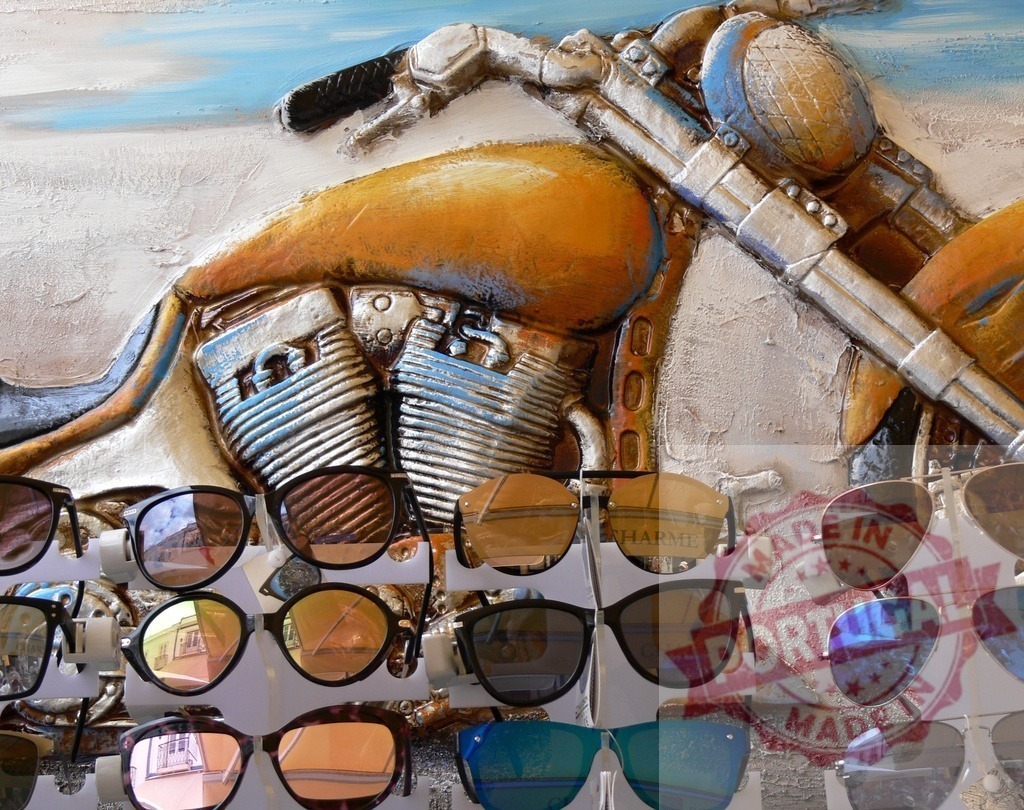 Sunglasses reflecting street market and motorcycle bas-relief art | Sunglasses displayed in a street market, reflecting surroundings against a motorcycle bas-relief - Realized with Pictrs.com