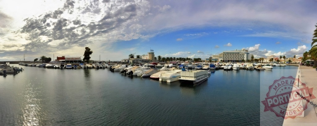 Faro marina with boats docked under cloudy sky | Faro marina filled with boats, buildings and palm trees under a partly cloudy sky - Realized with Pictrs.com
