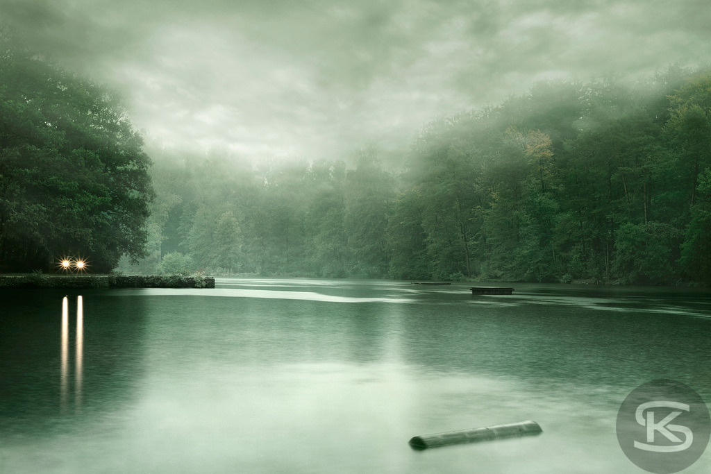 Mystischer nebliger Waldsee in düsterer Stimmung | Tauchen Sie ein in die geheimnisvolle Atmosphäre dieses nebligen Waldsees. Das Bild fängt die stille, fast unheimliche Stimmung der Natur ein, mit verschwommenen Baumrändern im Hintergrund und einer spiegelglatten Wasseroberfläche, die nur von leichten Regentropfen gestört wird. Entdecken Sie die fesselnde Farbpalette aus Grün, Grau und Dunkel, die diesem Ort eine einzigartige Tiefe verleiht. - Realisiert mit Pictrs.com