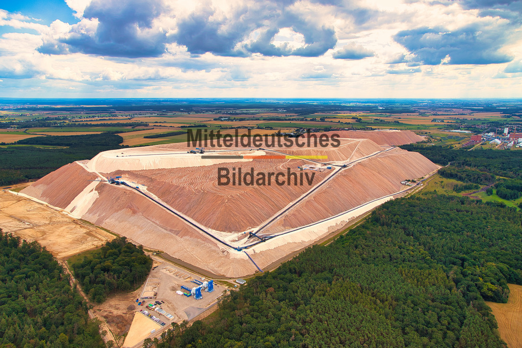 Kalimandscharo_Zielitz_Kalihalde_7352 | Das Luftbild zeigt den Kalimandscharo bei Zielitz aus einer Drohnenperspektive. Die schneeweiße, rötliche Kalihalde wirkt aus der Luft nahezu geometrisch und hebt sich mit ihren klaren Kanten und regelmäßigen Böschungen deutlich von der umgebenden Landschaft ab. Die außergewöhnliche Form macht die Halde zu einem markanten technischen Bauwerk, das schon aus großer Entfernung sichtbar ist.Der Kalimandscharo ist die Rückstandshalde des Kaliwerks Zielitz, des größten Kalibergwerks Deutschlands. Die Halde erreicht eine Höhe von rund 120 Metern über dem umliegenden Gelände beziehungsweise etwa 200 Meter über dem Meeresspiegel und besitzt eine Grundfläche von rund 110 Hektar. Sie entsteht durch die Ablagerung von Rückständen aus der Kaliproduktion, bei der jährlich rund 12 Millionen Tonnen Rohsalz gefördert und verarbeitet werden.Die Drohnenaufnahme verdeutlicht eindrucksvoll die nahezu geometrische Form der Halde und ihre technischen Dimensionen. Das Luftbild dokumentiert eines der markantesten Zeugnisse des Kalibergbaus in Deutschland und zeigt, wie moderne Rohstoffgewinnung das Landschaftsbild nachhaltig prägt. - Realisiert mit Pictrs.com