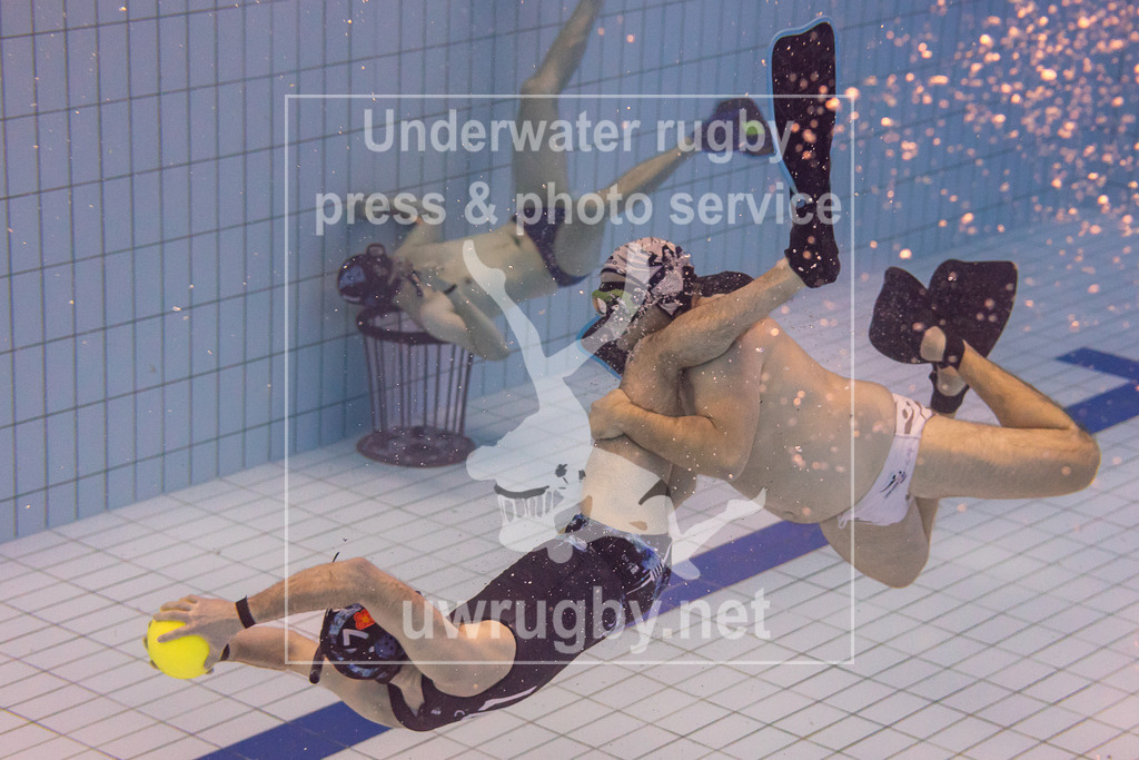 TC Stuttgart vs, TSV Malsch, Unterwasser-Rugby, 1. Bundesliga Süd, 5. Spieltag, 2024/2025, 23.03.2025 | TC Stuttgart (blau) vs, TSV Malsch (weiß).  Ein Stuttgarter Spieler wird von einem Malscher Spieler gehalten. Im Hintergrund das Tor der Stuttgarter mit dem Torwart. - Realisiert mit Pictrs.com