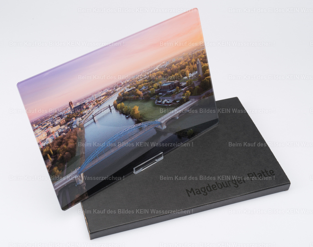 luftbild-magdeburg-verpackung-magdeburger-platte-steffen-lehmann | Ein Luftbild der Magdeburger Sternbrücke bei einem rosa gefärbten Sonnenaufgang – verpackt in einer eigens entwickelten schwarzen Pappverpackung.Für die Verpackung habe ich damals gemeinsam mit einem Magdeburger Start-up eine eigene Lösung entwickelt. Eine weitere Idee war der Aufdruck „Magdeburger Platte®“ auf der Verpackung. Das sah zwar sehr edel aus und gab dem Präsent einen hochwertigen Auftritt, hatte aber auch einen kleinen Nachteil: Die eigentliche Platte war von außen nicht zu sehen.Auch solche Versuche gehörten zur Entwicklung der „Magdeburger Platte®“ dazu – ausprobieren, verbessern und schauen, was in der Praxis funktioniert. - Realisiert mit Pictrs.com