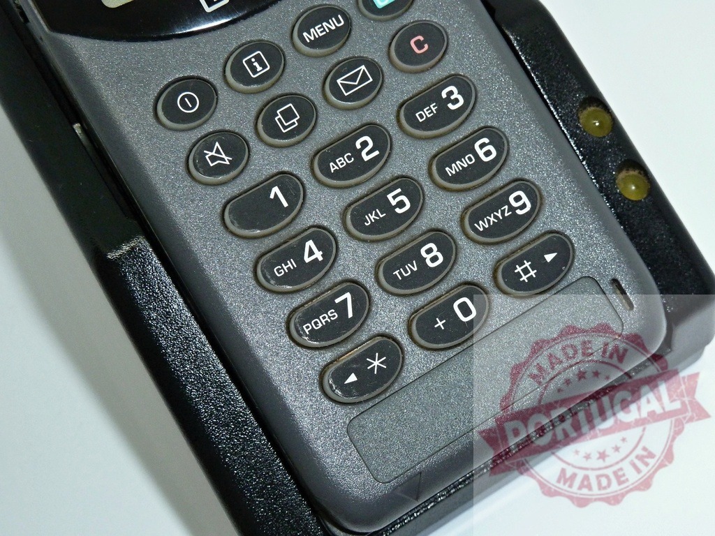Old Cell Phone Charging in Cradle Showing Keypad | Close-up of an old gray cell phone sitting in its charging cradle, highlighting the numbered keypad and menu buttons - Realisiert mit Pictrs.com