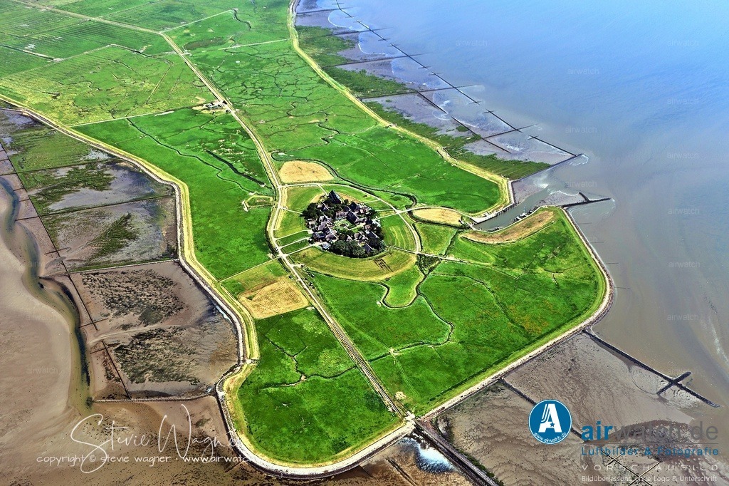 Der Damm zwischen der Hallig Oland und Langeneß ist eine 900 mm-spurige Feldbahn - Luftbild | Der Damm zwischen der Hallig Oland und Langeneß ist eine 900 mm-spurige Feldbahn, die als private Werkbahn des Landesamtes für Küstenschutz, Nationalpark und Meeresschutz (LKN) dient und ursprünglich 1928 fertiggestellt wurde.  Durch eine Erhöhung des Damms um 65 cm zwischen 2000 und 2013 ist die Strecke tideunabhängig befahrbar, was Fahrten unabhängig von Ebbe und Flut ermöglicht (außer bei extremen Sturmfluten oder Eis). 