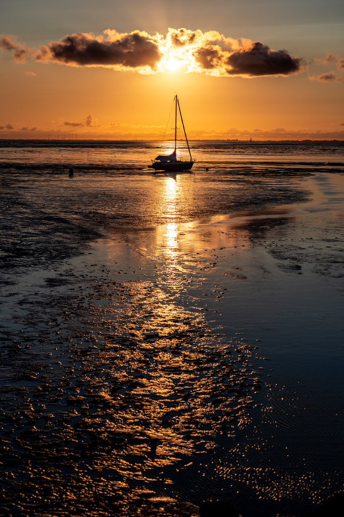 Watt ne Aussicht | Es ist Ebbe, die Sonne geht unter und ein einzelnes Boot liegt vor der Promenade im Watt.