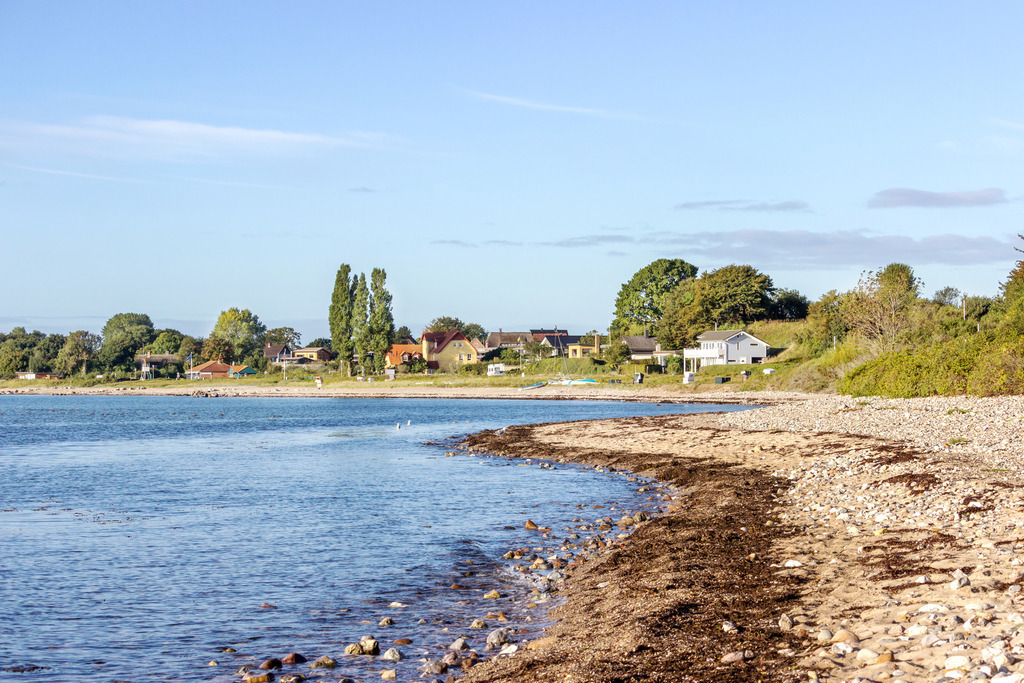 Wandbild: Strand in Langholz im Herbst | Dieses Wandbild im Querformat zeigt den Blick auf Langholz vom Naturstrand aus. Die Bäume in Langholz leuchten in schönen Herbstfarben. Am blauen Himmel befinden sich nur wenige kleine Wolken.  - Realisiert mit Pictrs.com