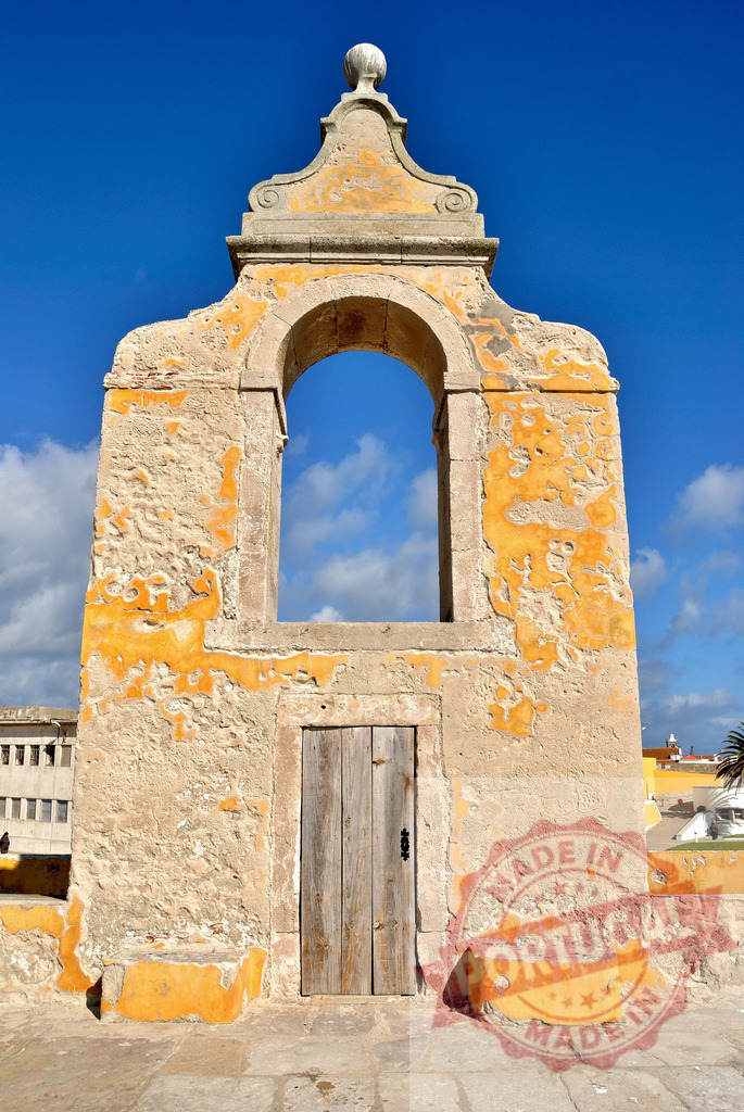 Peniche fortress architectural detail with arch and door. Centro - Portugal | Historic stone archway and small wooden door on the weathered fortress wall against blue sky - Realized with Pictrs.com