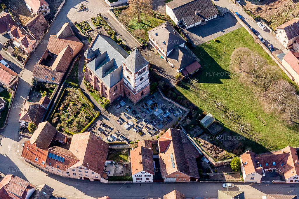 Aerial view: Church building and cemetery of the Église protestante luthérienne in the village center in Schwindratzheim in the state Bas-Rhin, France. – Photo: IMG_097609.jpg taken on 03/16/2017 by Werner Riehm/FLY-FOTO.com – Resolution of the original: 3817 x 2545 px