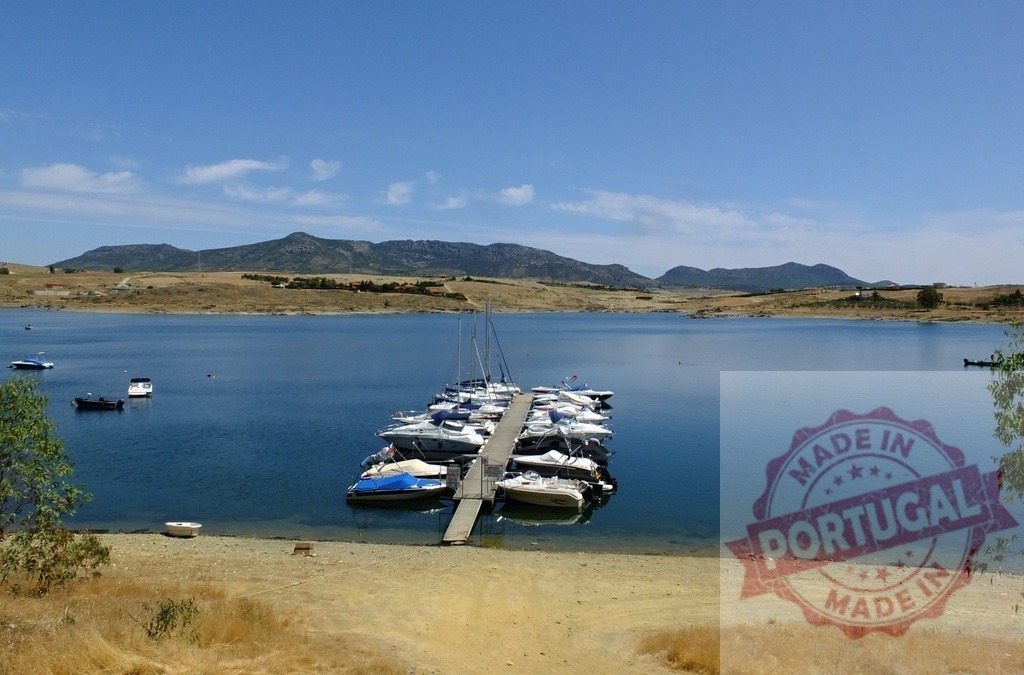 Boats moored at wooden dock on calm lake. Spain - Extremadura | Recreational boats moored at a dock on clear blue lake with mountains under a summer sky - Realized with Pictrs.com