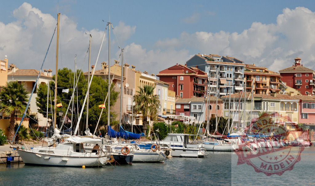 Sailboats mooring in Empuriabrava, Spain, creating a picturesque marina view | White sailboats are creating a picturesque marina view in front of colorful residential buildings in Empuriabrava, Spain - Realized with Pictrs.com