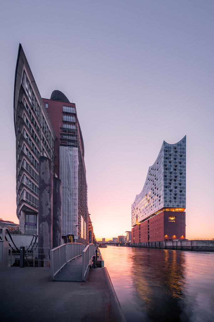 Elbphilharmonie am Wasser der HafenCity | Die Elbphilharmonie erhebt sich zwischen moderner Architektur und den Wasserflächen der Hamburger HafenCity während der Morgendämmerung. - Realisiert mit Pictrs.com