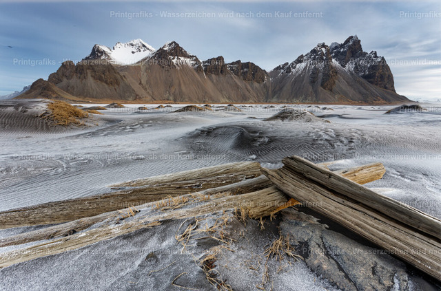Vestrahorn hinter schwarzem Sand | Die markante Bergkette des Vestrahorn erhebt sich hinter schwarzem Sand, verwehtem Strandgras und altem Treibholz. Die kühle Farbwirkung, die Strukturen im Sand und die dramatische Kulisse zeigen die raue Schönheit von Stokksnes in Island. - Realisiert mit Pictrs.com