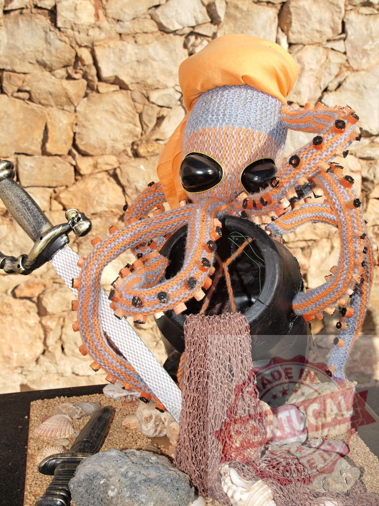 Knitted octopus pirate looking for buried treasure | Handcrafted octopus pirate toy guarding a black cauldron filled with sandy treasure - Realized with Pictrs.com