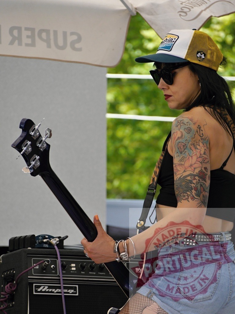 Female musician playing bass guitar with tattoos | Female musician performing live music, wearing sunglasses and showing arm tattoos - Realisiert mit Pictrs.com