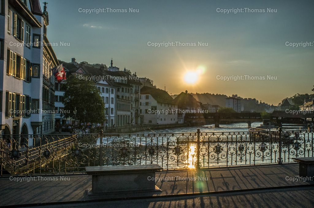 altstadt-luzern-sonnenuntergang-2 | „Blick von einer Brücke über die Reuss in Luzern bei Sonnenuntergang, Schweizer Flagge an einem Gebäude.“