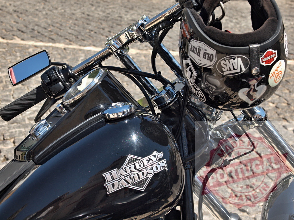 Harley-Davidson motorcycle with helmet showcasing riding lifestyle | Black Harley-Davidson motorcycle parked outdoors with a sticker-covered helmet resting on the handlebars - Realisiert mit Pictrs.com