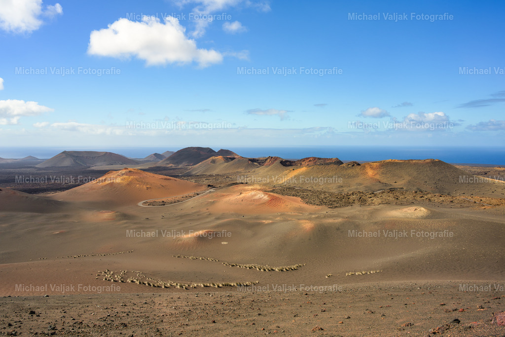 Vulkanlandschaft im Timanfaya Nationalpark auf Lanzarote | Über den weiten Kratern und rötlichen Aschefeldern des Timanfaya Nationalparks spannt sich ein klarer Himmel. Eine einzelne Wolke zieht kontrastreich darüber hinweg und verstärkt die Wirkung der kargen Landschaft.Die warmen Erdtöne – von Rostrot bis Ocker – stehen im spannungsvollen Gegensatz zum hellen Blau des Himmels. So entsteht ein Bild von Ruhe und Weite, in dem die vulkanische Vergangenheit Lanzarotes und die Leichtigkeit des Himmels miteinander verschmelzen. - Realisiert mit Pictrs.com