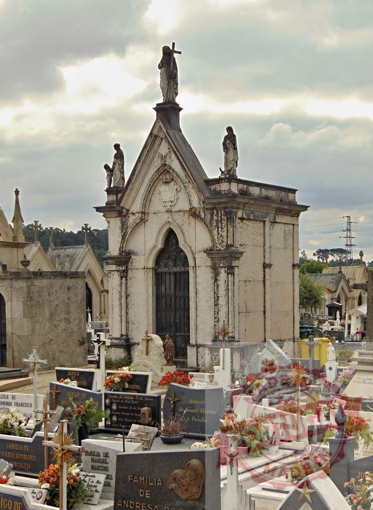 Old cemetery mausoleum with statues and gravestones under cloudy sky. Region Norte - Portugal | Ornate chapel-like mausoleum with religious statues surrounded by graves and crosses - Realized with Pictrs.com