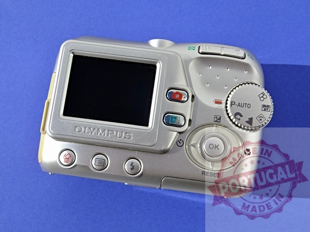 Olympus vintage silver digital camera on blue background | Olympus vintage silver digital camera back view showing screen and controls - Realisiert mit Pictrs.com