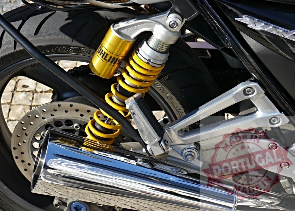 Motorcycle rear wheel showing Ohlins suspension and exhaust pipe | Motorcycle rear wheel detailing premium Ohlins shock absorber, brake disc, and chrome exhaust - Realized with Pictrs.com