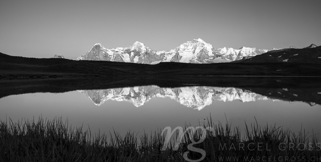 Spiegelung von Eiger, Mönch und Jungfrau in Bergsee während Sonnenuntergang | Die ideale Geschenkidee für Naturliebhaber. Naturbilder von Marcel Gross Photography für ihr Zuhause in den verschiedensten Formaten und Materialien. - Realisiert mit Pictrs.com