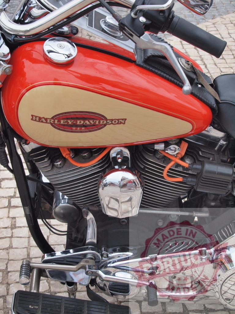 Harley-Davidson motorcycle engine with chrome details | Harley-Davidson gas tank and engine with chrome finish and orange cables parked on cobblestones - Realized with Pictrs.com