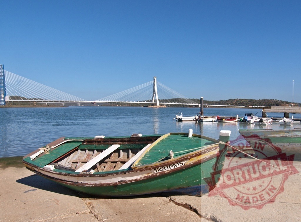 Fishing boat with Guadiana International Bridge in Portugal | Old fishing boat resting on riverbank with a modern cable-stayed bridge spanning the river - Realized with Pictrs.com