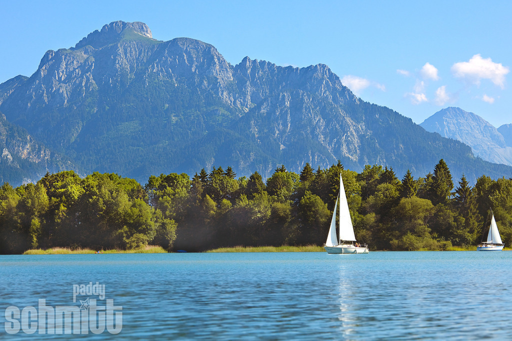 Segelboot auf dem Forggensee vor dem Säuling | Ein Segelboot gleitet über den Forggensee, während sich der markante Säuling majestätisch im Hintergrund erhebt. Eine stimmungsvolle Aufnahme aus der Region Füssen im Ostallgäu, die See, Berge und den besonderen Charme der Allgäuer Landschaft vereint. - Realisiert mit Pictrs.com