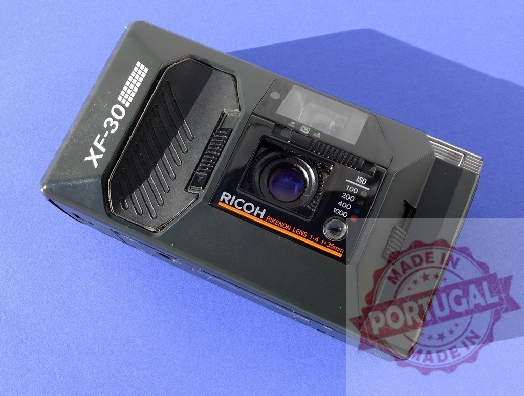 Ricoh XF-30 compact film camera flat laying on blue | Vintage Ricoh XF-30 point and shoot film camera displaying analog photography technology - Realized with Pictrs.com