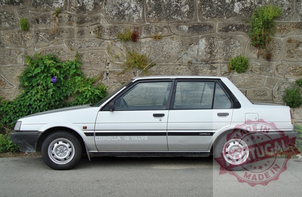 Silver Toyota Corolla parked near stone wall with vegetation growing on it | Classic silver Toyota Corolla 12 valve parked on the side of the road by a stone wall with vegetation growing on it - Realisiert mit Pictrs.com