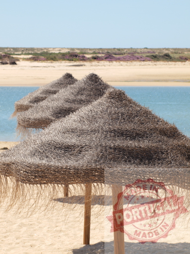 Straw umbrellas providing shade on sandy beach | Straw umbrellas offering shade on a sunny beach with calm water and sand in the background - Realized with Pictrs.com