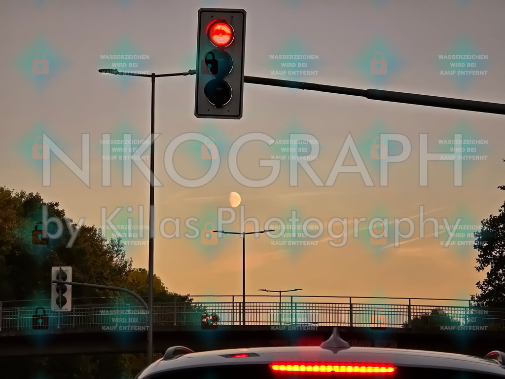 Rotes Licht, silberner Mond – Ein Moment der Stille in Iserlohn | Ein stimmungsvolles Straßenbild bei Dämmerung, aufgenommen an der Seilerseestr. in Iserlohn, Deutschland – einer Stadt im Sauerland, geprägt von sanften Hügeln, grünen Rändern und einer Mischung aus ländlicher Ruhe und städtischer Infrastruktur. Im Vordergrund leuchtet ein rotes Ampellicht – klar, ruhig, unübersehbar – an einem Mast über einer Straße, auf der ein Auto mit eingeschaltetem Bremslicht wartet. Im Hintergrund, zwischen Straßenlaternen und einer Brücke, schwebt der Mond als schmaler, heller Sichel am leicht bewölkten Himmel – fast wie ein stilles, himmlisches Gegenlicht zum roten Signal. Grüne Bäume säumen die Straße, und die Farbpalette aus Grau, Rot und sanftem Abendgold verleiht der Szene eine melancholisch-poetische Atmosphäre. Es ist ein Moment der Stille im Alltag: wo Verkehr und Natur sich begegnen, wo die Stadt kurz innehält – und der Himmel still zuschaut.Dieses Bild ist bei nikograph.eu erhältlich und kann als verschiedene Fotoprodukte bestellt werden – ideal für Wohnzimmer, Büro, oder als Geschenk für Menschen, die die Schönheit des Alltags schätzen:Gerahmter Kunstdruck – in verschiedenen Rahmendesigns und GrößenLeinwandbild – für eine künstlerische, texturierte WirkungPoster – leicht, modern und wandfreundlichAcrylglasbild – glänzend, tief und detailreichAlu-Dibond – edel, robust und zeitlosFoto-Tasse, Mousepad, Kalender oder Notizbuch – als praktisches und persönliches GeschenkAlle Produkte sind in verschiedenen Formaten und Größen verfügbar – von kleinen Wandbildern bis zu XXL-Drucken.