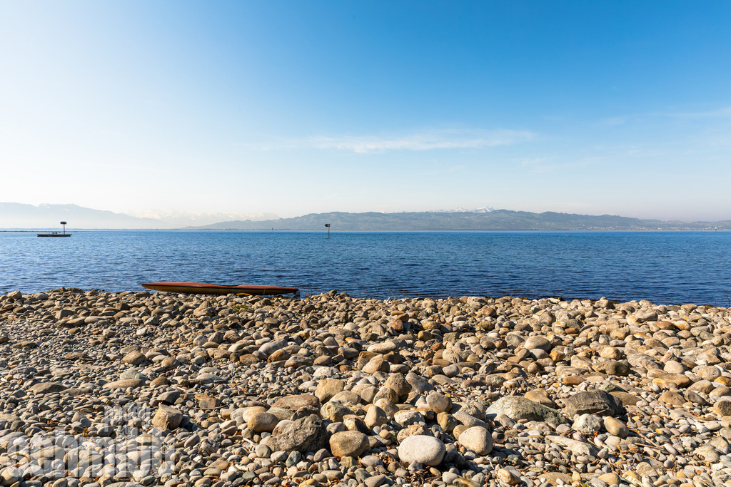 Bergpanorama am Seeufer bei Wasserburg am Bodensee | Am Seeufer bei Wasserburg eröffnet sich ein weiter Blick über den Bodensee bis zur beeindruckenden Bergkulisse am Horizont. Das ruhige Wasser und die majestätischen Berge verbinden sich zu einem harmonischen Panorama, das die besondere Schönheit der Bodenseelandschaft einfängt. - Realisiert mit Pictrs.com