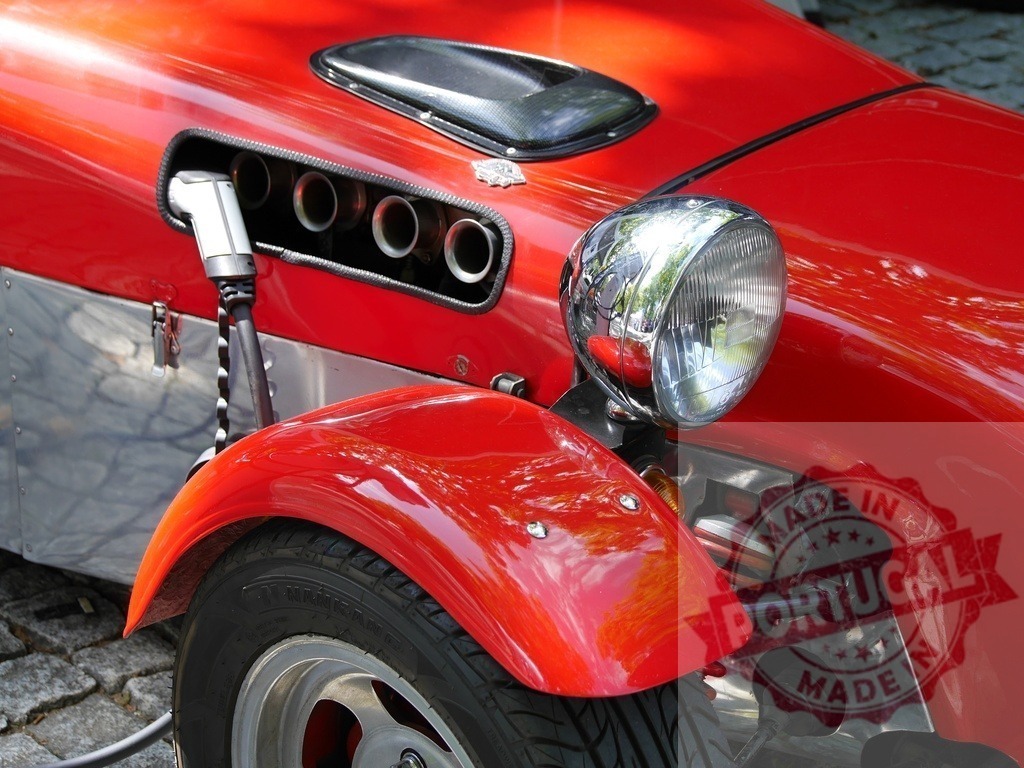 Red vintage electric sports car charging | Red vintage-style sports car plugging in for an electric charge on a cobblestone street - Realized with Pictrs.com