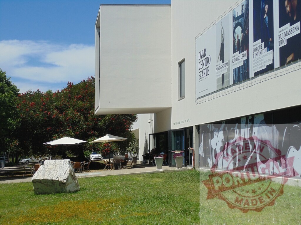 Ovar Centro de Arte building with posters and outdoor cafe. Aveiro - Portugal | Modern architecture of Ovar Centro de Arte with a relaxing outdoor cafe and green lawn - Realized with Pictrs.com
