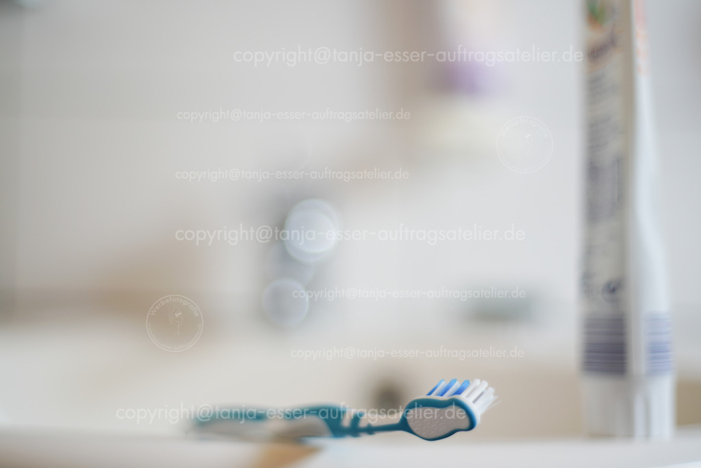 Tooth brush at bathroom 1 D | Zahnbürste im Fokus, im uscharfen Hintergrund ist Zahnpasta und ein Badezimmer. Viel Copy Space zum Thema Mundgesundheit.