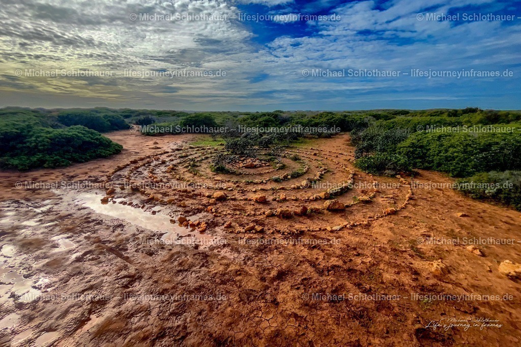 SpiralfÃ¶rmiges Steinlabyrinth an der Algarve | Ein spiralfÃ¶rmig angelegtes Steinlabyrinth in der rÃ¶tlichen KÃ¼stenlandschaft der Algarve, umgeben von grÃ¼ner Macchia. - Realisiert mit Pictrs.com