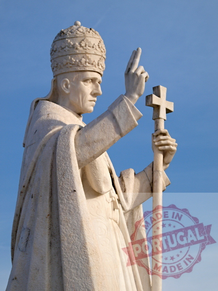Pope John Paul II statue blessing with cross against blue sky | Marble statue of Pope John Paul II holding a cross and blessing, with a clear blue sky in the background - Realisiert mit Pictrs.com