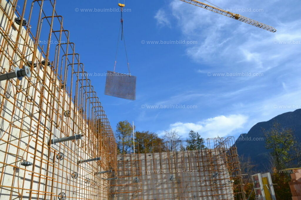 Bewehrung Betonwand | Außenschalung und Bewehrung für Betonwand, dahinter Baukran mit schwebenden Baustahlmatten, Hintergrund blauer Himmel 