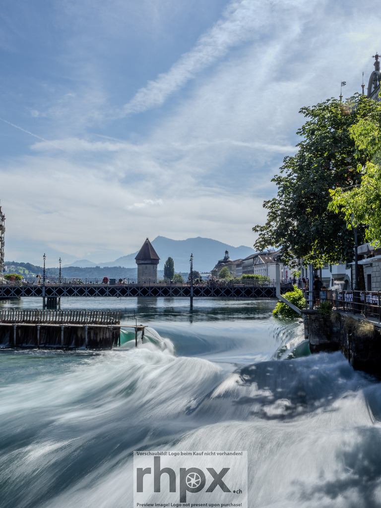 Reuss Luzern – Blick auf die Altstadt | Fliesskraft. Geschichte. Bergblick.Die Reuss in Luzern zeigt ihre Kraft, während das aufgewühlte Wasser in langen Belichtungszeiten zu seidiger Textur verschwimmt. Im Hintergrund wacht die historische Kapellbrücke mit ihrem ikonischen Wasserturm über die Szene, eingerahmt vom grünen Ufer und der majestätischen Alpenkulisse.Wähle unter "Produktauswahl" dein Wunschformat: Vom klassischen Wandbild über Puzzle &amp; Tassen bis zum digitalen Download (z.B. als Handy-Hintergrund). - Realisiert mit Pictrs.com
