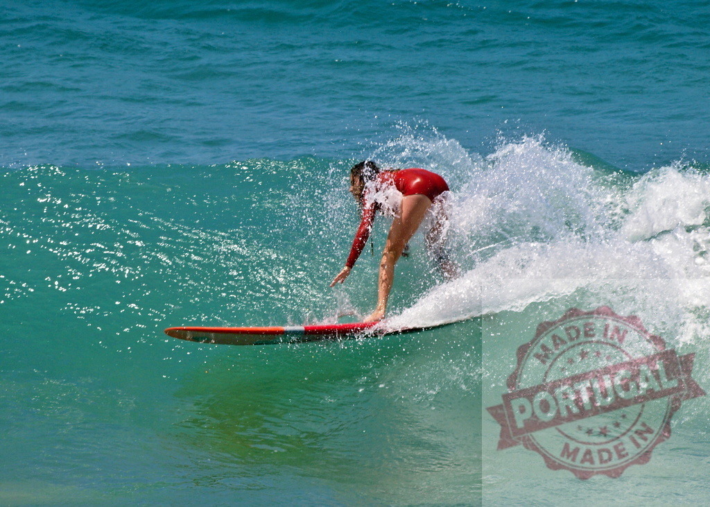 Female surfer riding a wave on a longboard in turquoise water | Professional surfer riding a wave on a longboard in a red wetsuit - Realized with Pictrs.com
