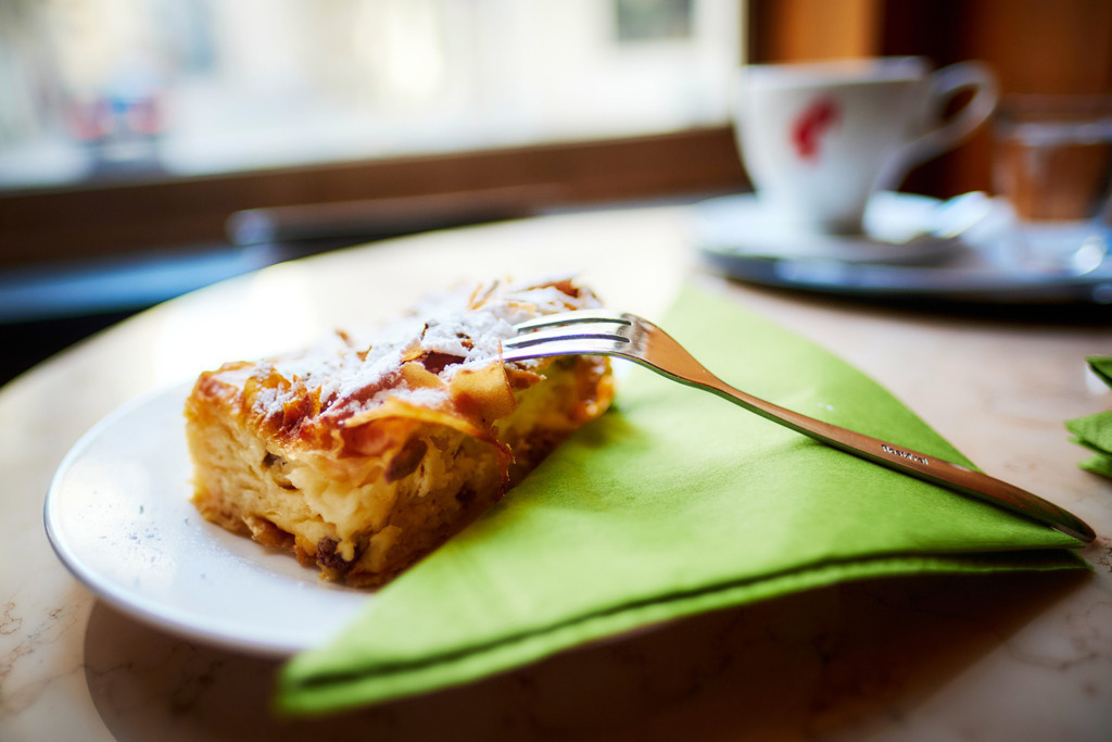 Cafe Volkstheater | WIen, Austria - February 20, 2020: Cafe Volkstheater; ein Stück Topfenstrudel auf dem Teller mit einer grünen Serviette, im Hintergrund eine Tasse Cafe. - Realisiert mit Pictrs.com