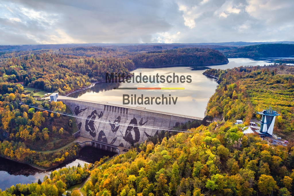 Rappbode Tallsperre Graffiti Harz Herbst-0026 | Das Luftbild zeigt die Staumauer der Rappbodetalsperre aus einer Drohnenperspektive. Die mächtige Betonstaumauer wird von einem großflächigen Schmetterlingsgraffiti geprägt, das einen eindrucksvollen Kontrast zur sachlichen Ingenieurarchitektur bildet. Aus der Vogelperspektive werden die Dimensionen des Bauwerks ebenso deutlich wie die außergewöhnliche Verbindung von technischer Funktion und moderner Street-Art.Die Rappbodetalsperre wurde zwischen 1952 und 1959 errichtet und ist mit einer Höhe von 106 Metern die höchste Staumauer Deutschlands. Die 415 Meter lange Gewichtsstaumauer staut bis zu 113 Millionen Kubikmeter Wasser und spielt eine zentrale Rolle für die Trinkwasserversorgung, den Hochwasserschutz und die Energieerzeugung im Harz. Das weithin sichtbare Schmetterlingsgraffiti wurde im Rahmen eines Kunstprojektes auf die Staumauer aufgebracht und zählt heute zu den markantesten Kunstwerken auf einem technischen Bauwerk in Deutschland.Die Drohnenaufnahme verdeutlicht eindrucksvoll die monumentalen Ausmaße der Staumauer und die Präzision ihrer Konstruktion. Das farbenfrohe Schmetterlingsmotiv setzt einen außergewöhnlichen gestalterischen Akzent und verbindet moderne Kunst mit einem der bedeutendsten wasserbaulichen Ingenieurwerke Deutschlands. - Realisiert mit Pictrs.com