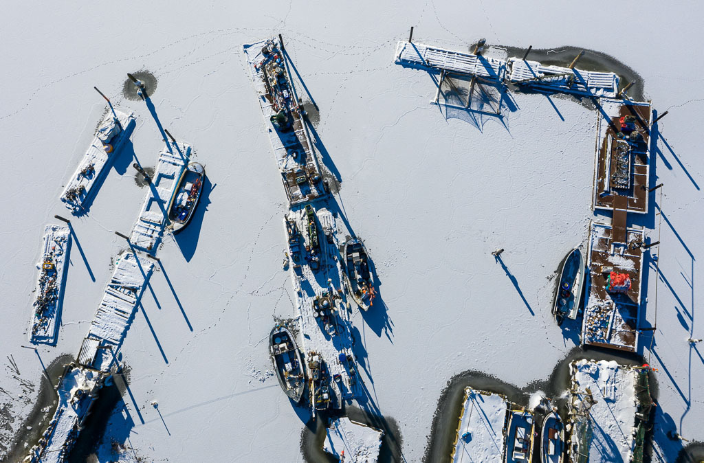 deutschland-2021-011 | Im Eis der Schlei: Landungsbrücken und Boote in der Fischersiedlung Holm in Schleswig aus der Vogelperspektive - Realisiert mit Pictrs.com