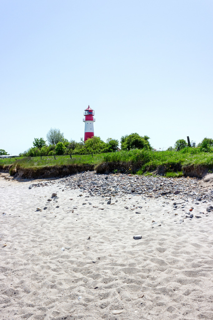 Wandbild: Leuchtturm in Falshöft  | Dieses Wandbild im Querformat zeigt den Leuchtturm in Falshöft im Frühling. Der blaue Himmel ist wolkenlos. Um den Leuchtturm befindet sich frisches Frühlingsgrün.  - Realisiert mit Pictrs.com