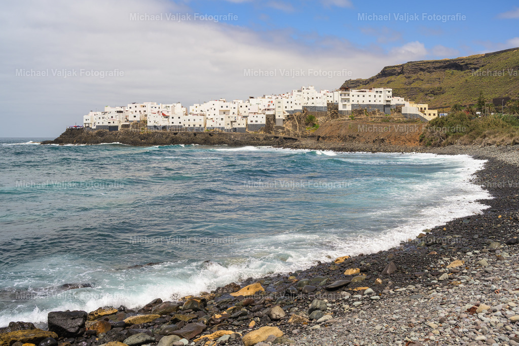 El Roque auf Gran Canaria | El Roque auf Gran Canaria ist ein malerisches Küstendorf, das sich spektakulär auf einem Basaltfelsen erhebt. Die weißen Häuser schmiegen sich eng aneinander und bieten einen atemberaubenden Blick auf den Atlantik. Die raue Schönheit des Ortes wird durch die kraftvollen Wellen unterstrichen, die gegen die Felsen schlagen.Dieser Ort verkörpert die Essenz traditioneller kanarischer Architektur und die Harmonie zwischen Mensch und Natur. Die schroffen Klippen, das tiefblaue Meer und die charmanten, verwinkelten Gassen erzählen die Geschichte eines Dorfes, das sich über Generationen hinweg den Herausforderungen des Ozeans gestellt hat und heute als verstecktes Juwel gilt. - Realisiert mit Pictrs.com