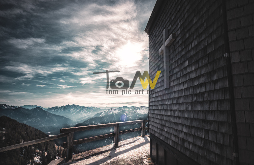 Blick an der Kirche vom Wallberg auf die Alpen---Tegernsee | Das Bild zeigt das Wallbergkircherl, auch bekannt als die St.-Quirin-Kapelle, am Wallberg in Bayern. Es ist das Wahrzeichen des Wallbergs, einem 1.722 Meter hohen Berg im Mangfallgebirge in den Bayerischen Voralpen. Die Kapelle ist ein beliebtes Fotomotiv und bietet einen fantastischen Ausblick auf das Tegernseer Tal und die umliegende Bergwelt.  - Realisiert mit Pictrs.com