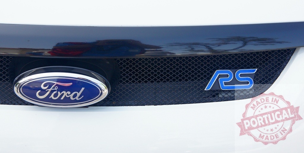 Ford Focus RS front grill featuring Ford logo and RS badge | Close-up of the front grill of a white Ford Focus RS, highlighting the Ford logo and the distinctive blue RS badge - Realized with Pictrs.com